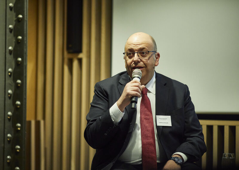 Tarek Chouman speaking at a financial technology conference, presenting to an audience with a microphone
